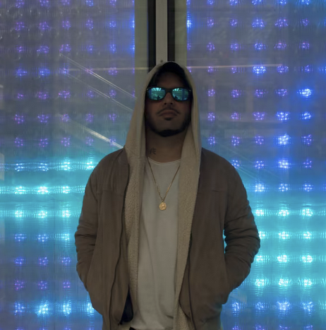 Van Paugam in a hooded jacket and sunglasses in front of blue lights in Paris